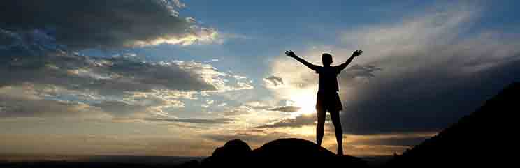 man standing with arms open in desert at sunset