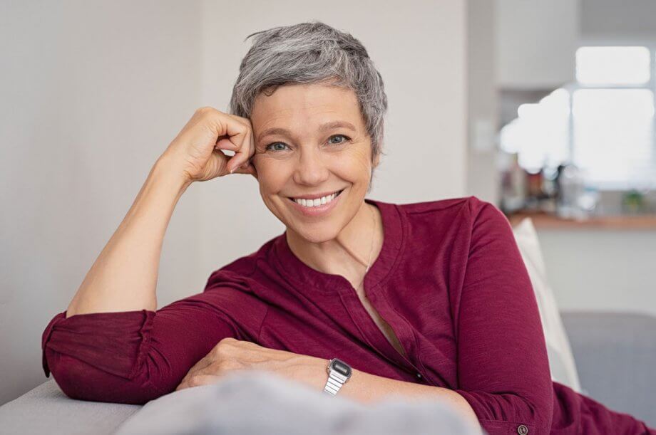 older woman in red shirt sitting on beige couch