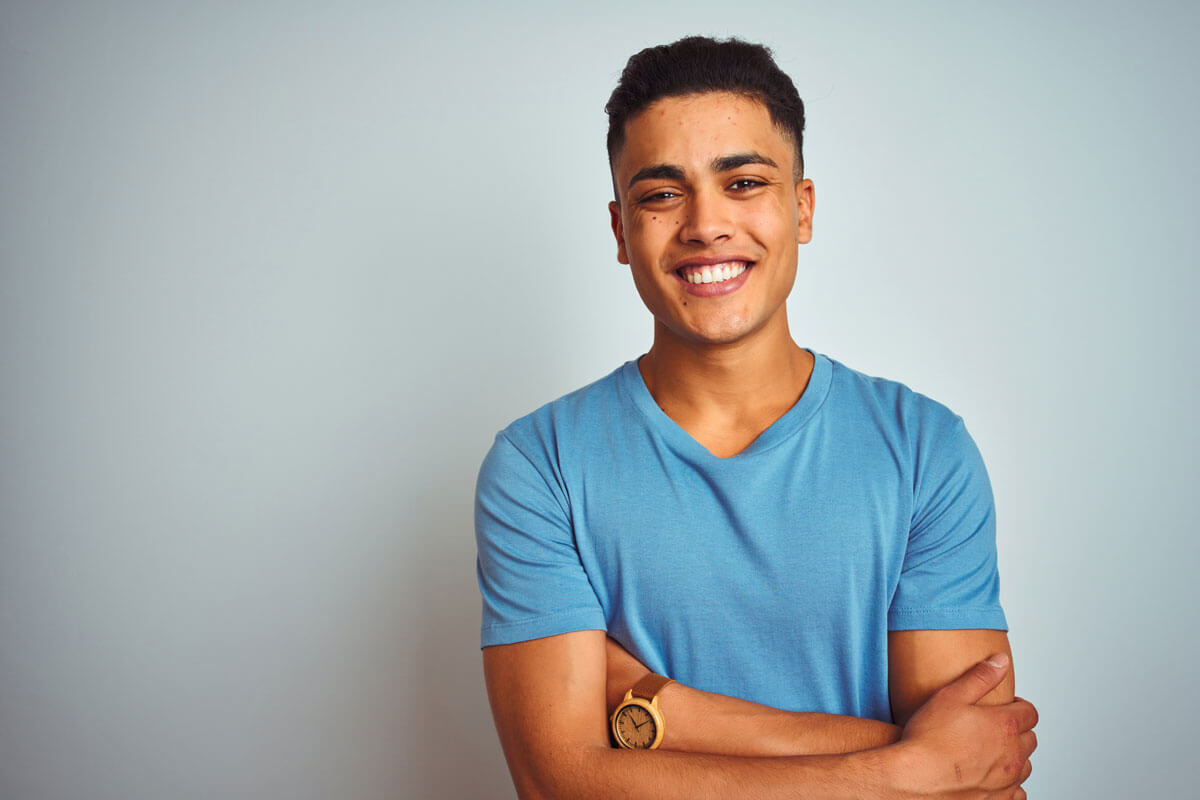 young man with arms crossed, smiling, standing against grey background